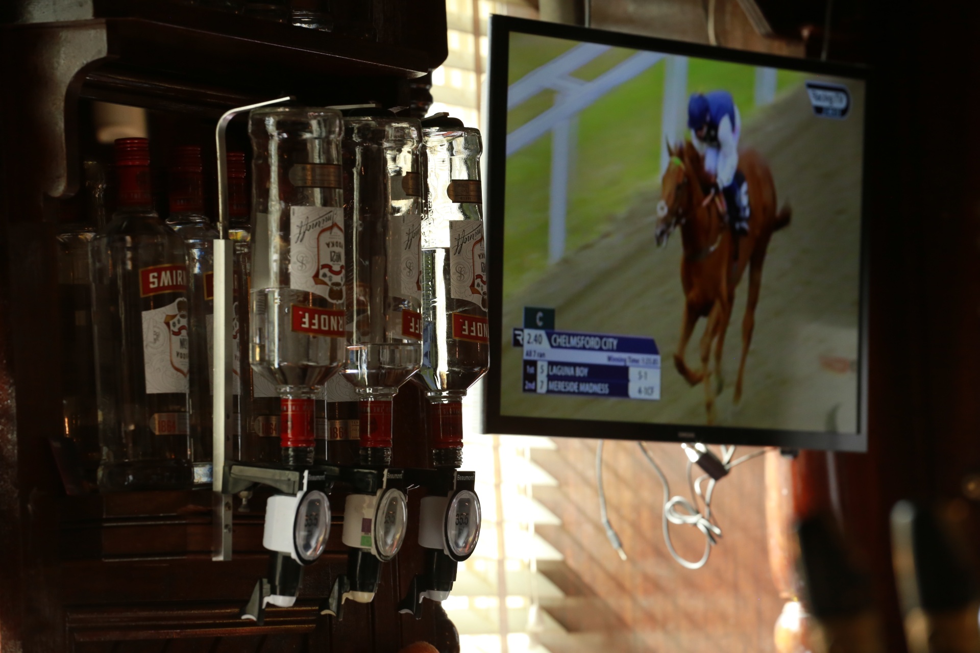 Vodka optics behind the bar with horse racing on the screen